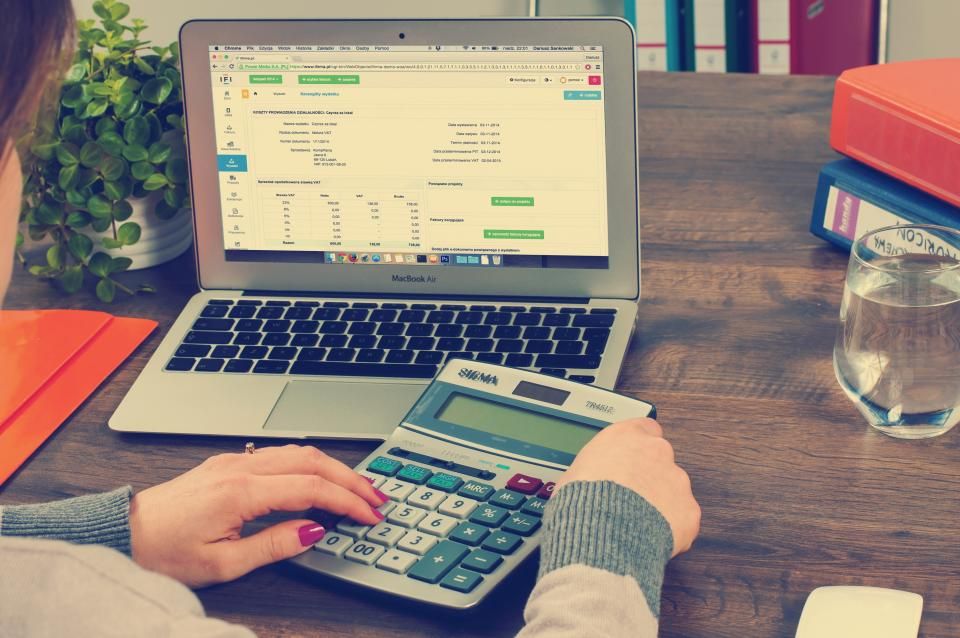Manos de una contadora usando calculadora frente a una laptop con una hoja de cálculo